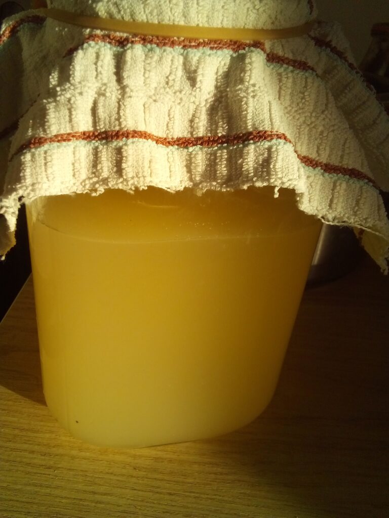 Wooden spoon stirring fermenting apples in glass jar for vinegar