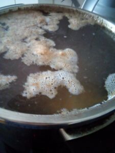 Beef bone broth gently boiling in a large pot with beef bones and vegetable remnants at the beginning of the cooking process using traditional homestead methods.