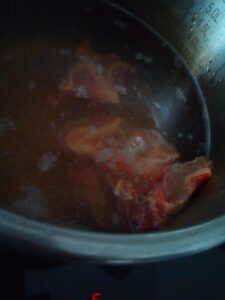 Slow simmered beef bone broth with visible bones and vegetable remnants during long cooking to extract collagen minerals and deep flavor.