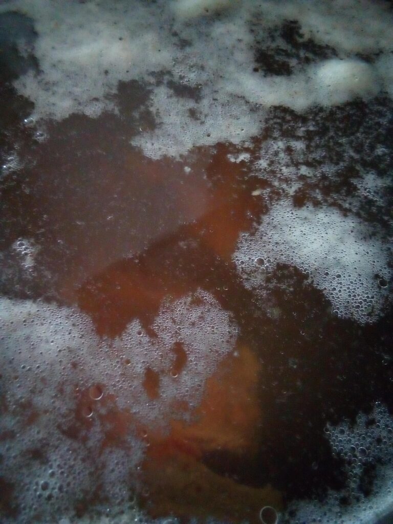 Homemade beef bone broth cooking low and slow with bones and leftover vegetables creating a clear nourishing broth for homestead kitchens.