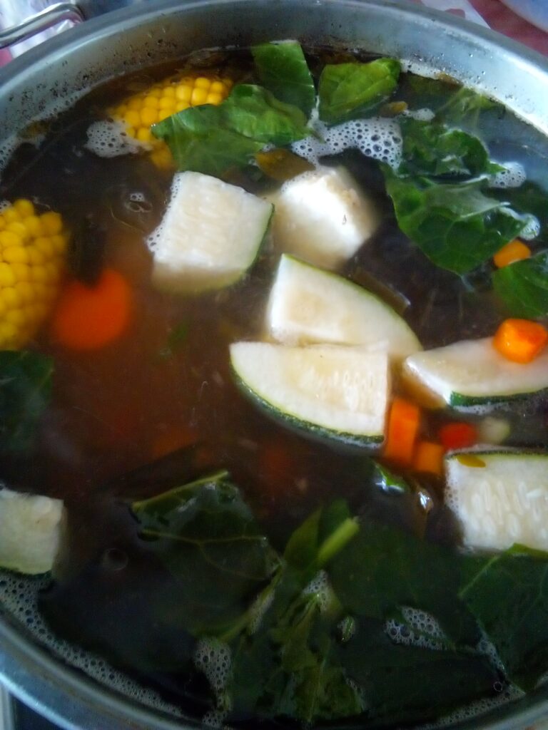 Beef soup slowly simmering in a large pot with bones and vegetables using traditional homestead cooking methods and low heat.