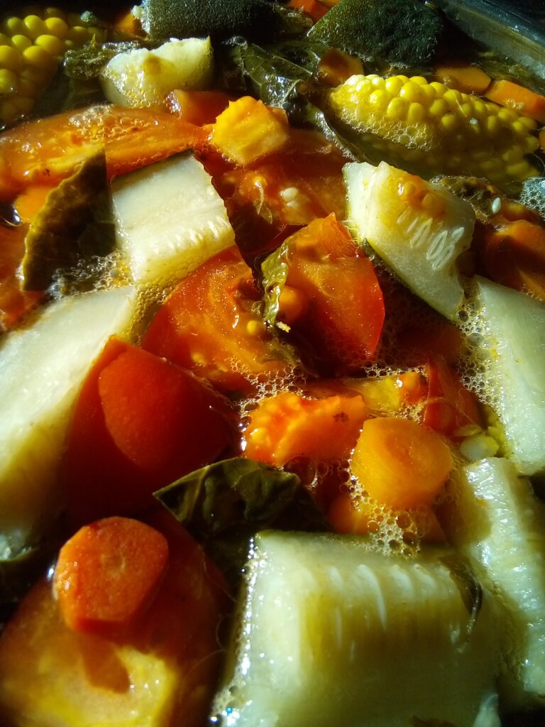 Sopa de res cocinándose a fuego lento en una olla grande con huesos y verduras para un caldo claro y nutritivo.